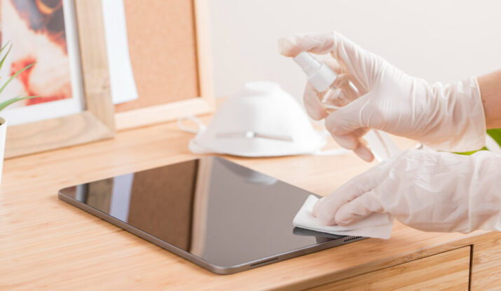 Cleaner in office sanitising and disinfecting a tablet