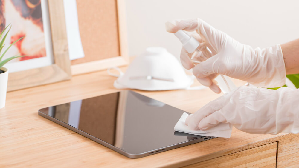 Cleaner in office sanitising and disinfecting a tablet
