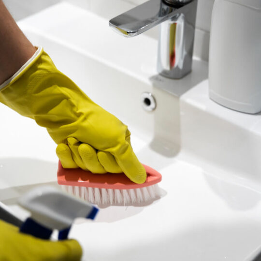 Office cleaner cleaning around a sink with a hard brush
