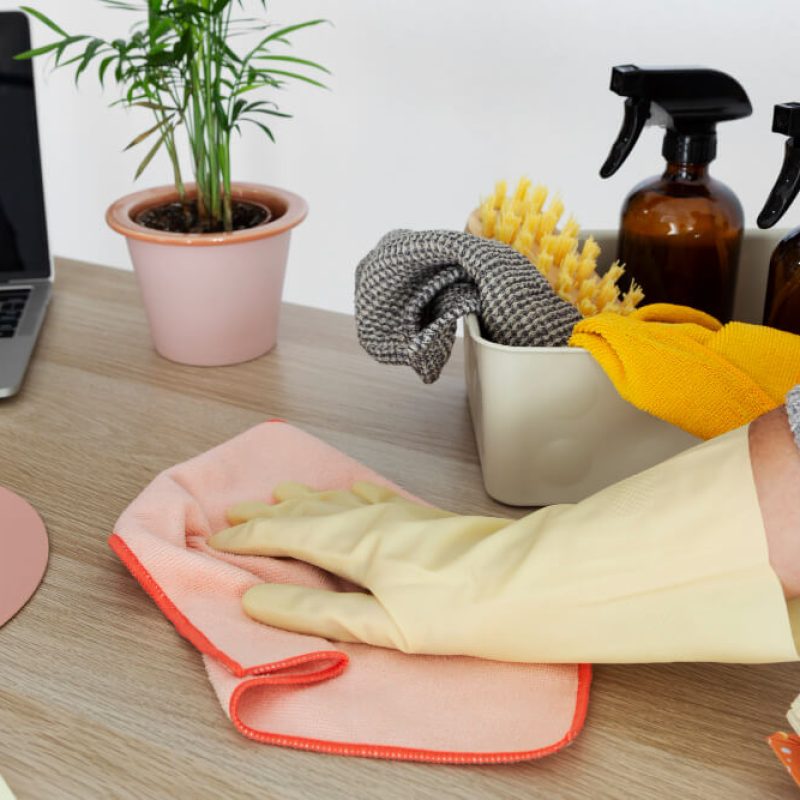 Office cleaner in gloves wiping a work desk with a clean microfibre cloth