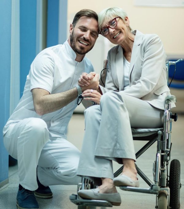 A happy elderly woman in a wheel chair with a doctor smiling together in a hospital