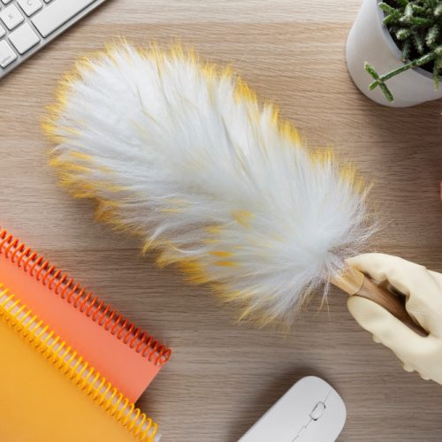Using feather duster to dust table as part of office cleaning services